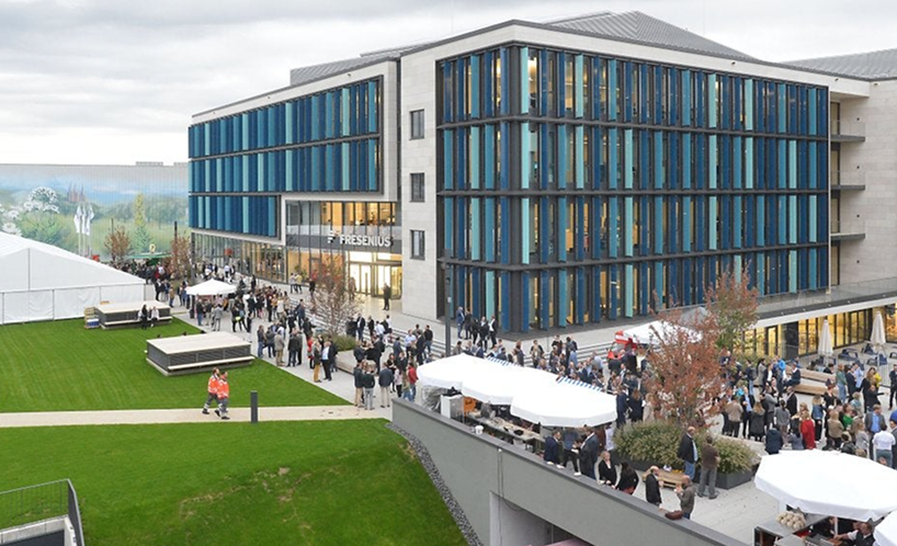 Fresenius campus building with modern blue glass windows and a large outdoor event gathering on the landscaped lawn