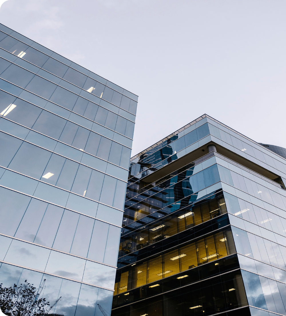Low-angle view of a modern glass skyscraper reflecting the sky and surrounding corporate buildings.