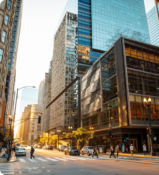 Modern city street featuring tall glass skyscrapers under a clear blue sky with pedestrians walking on the sidewalk