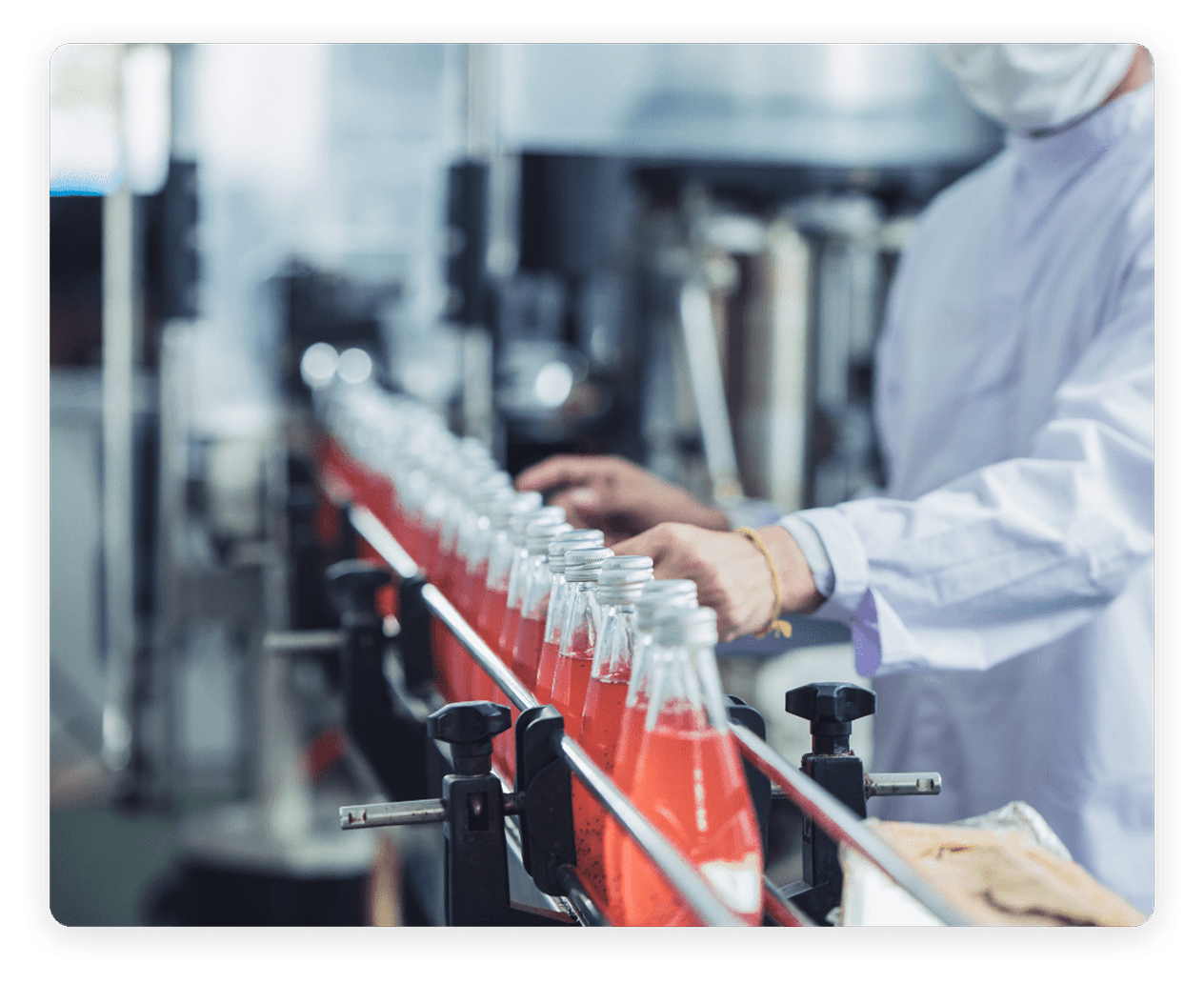 A worker in a lab coat and face mask inspecting products along an automated factory conveyor belt line.